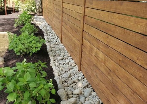 river rock bed and plantings along a backyard wood fence